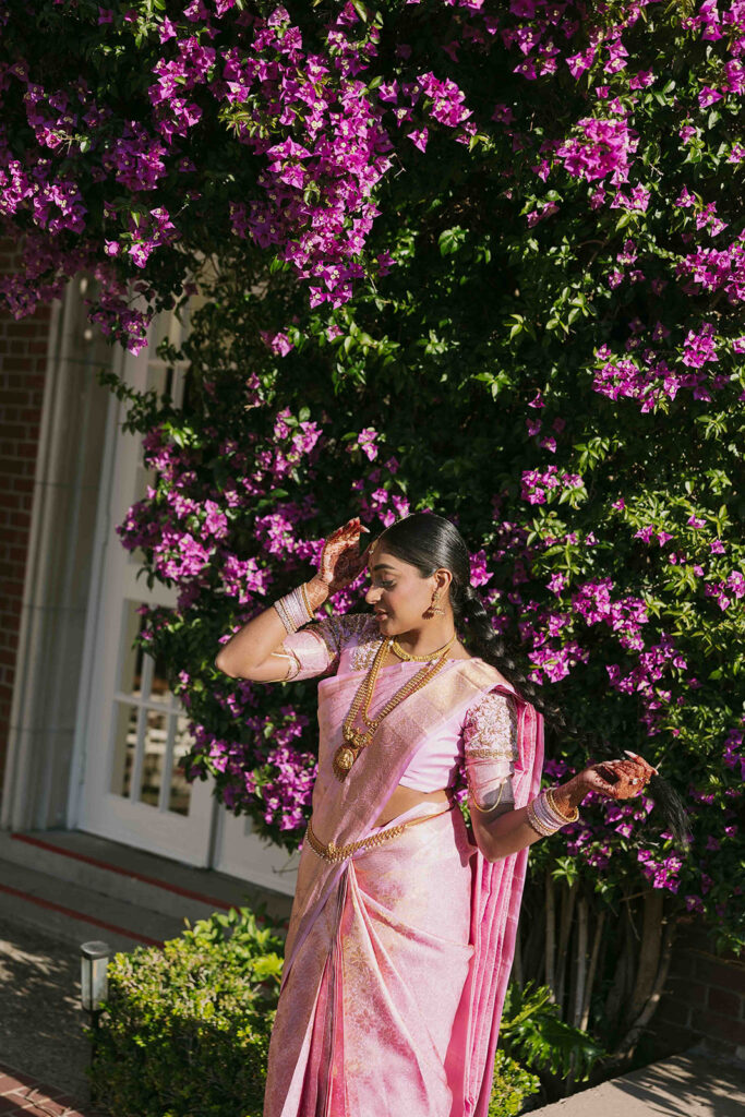 Bride in pink saree posing in front of bougainvillea.