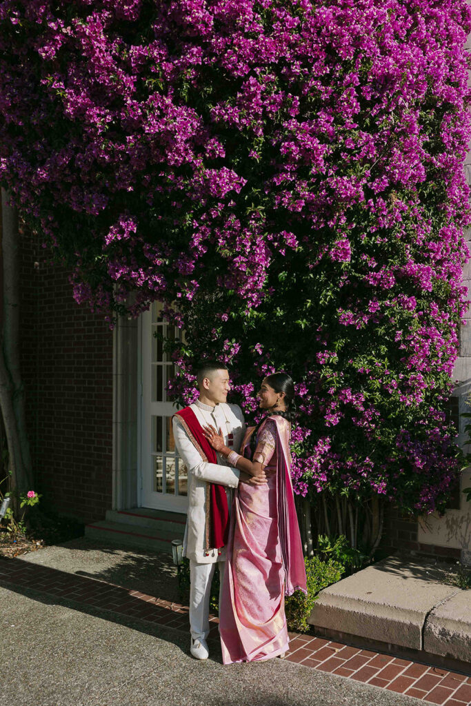 Bride and groom posing in front of a blooming deep purple bougainvillea.