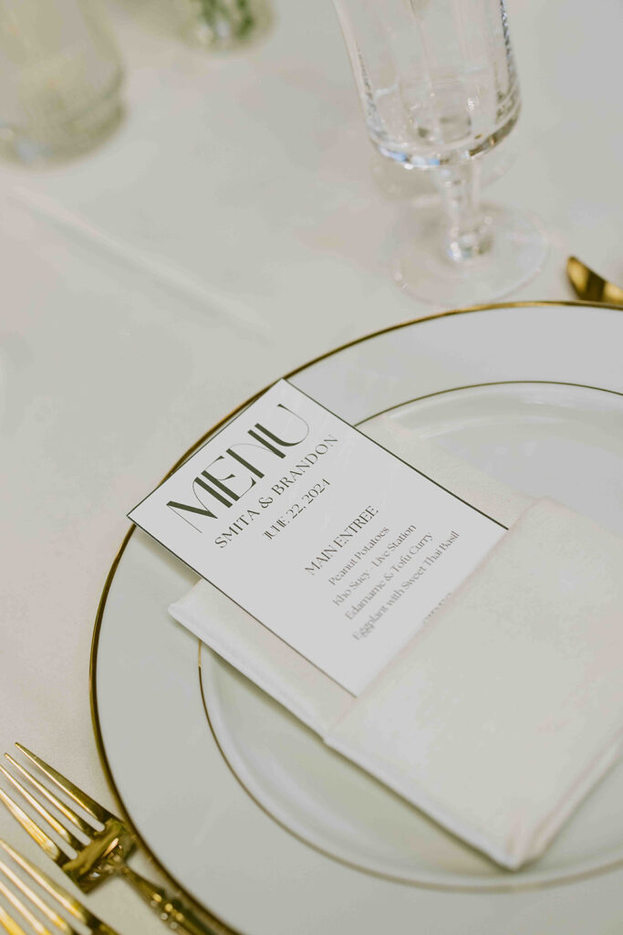 Menu on white and gold plate tucked into a folded white napkin.