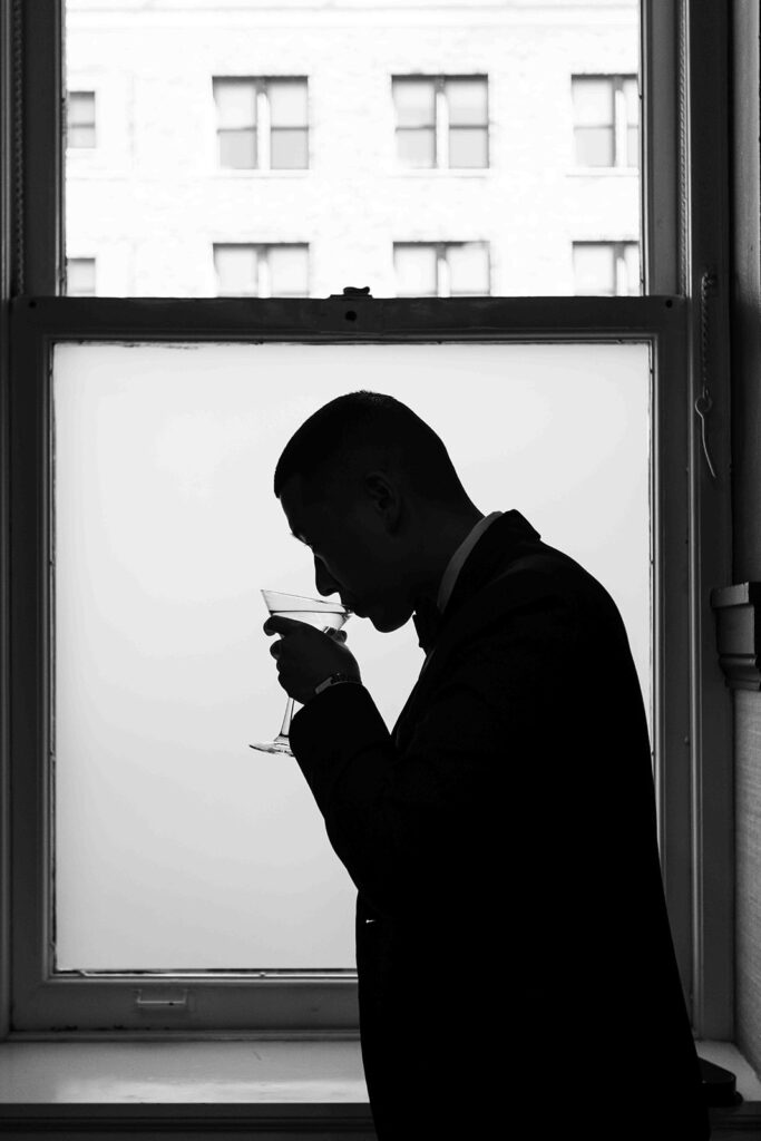 Silhouette photo of the groom sipping from a martini glass in front of a window.