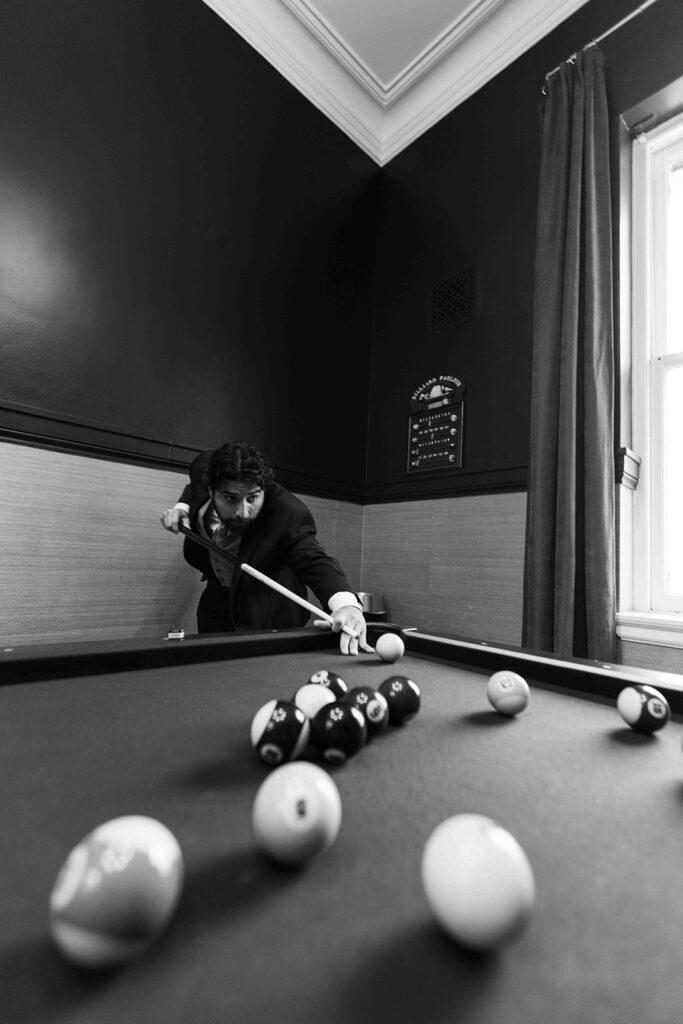 Groomsmen playing pool at the angle of the pool table in black and white.