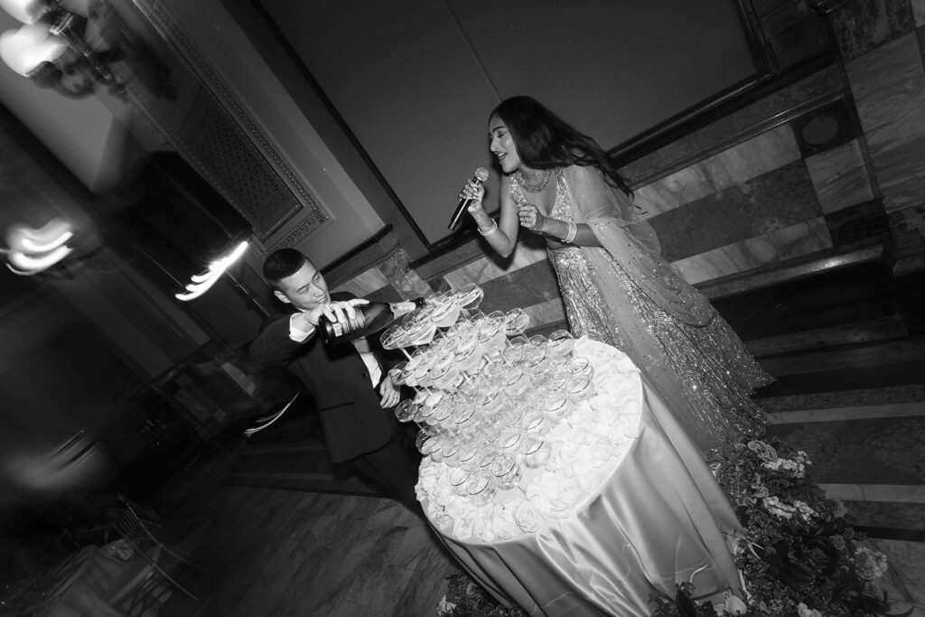 Groom pouring champagne over the coupe glass tower while the bride sings with a microphone.