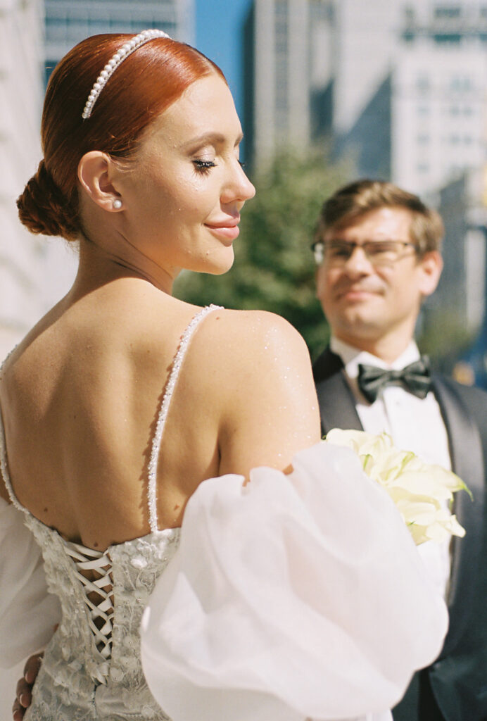 Bride looking over her shoulder while groom looks at her in he background.