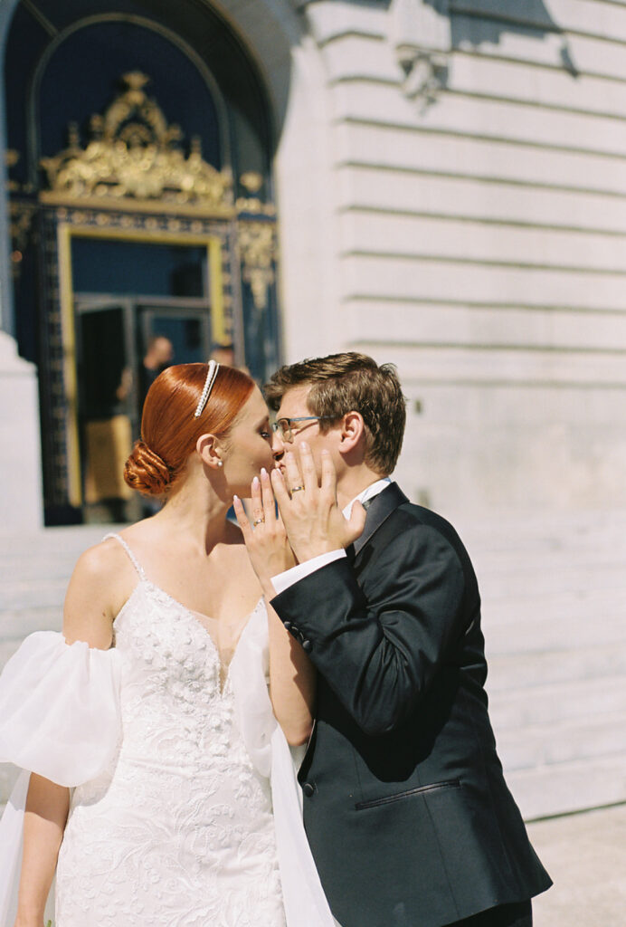 Bride and groom kiss in front of city hall while showing off their new rings