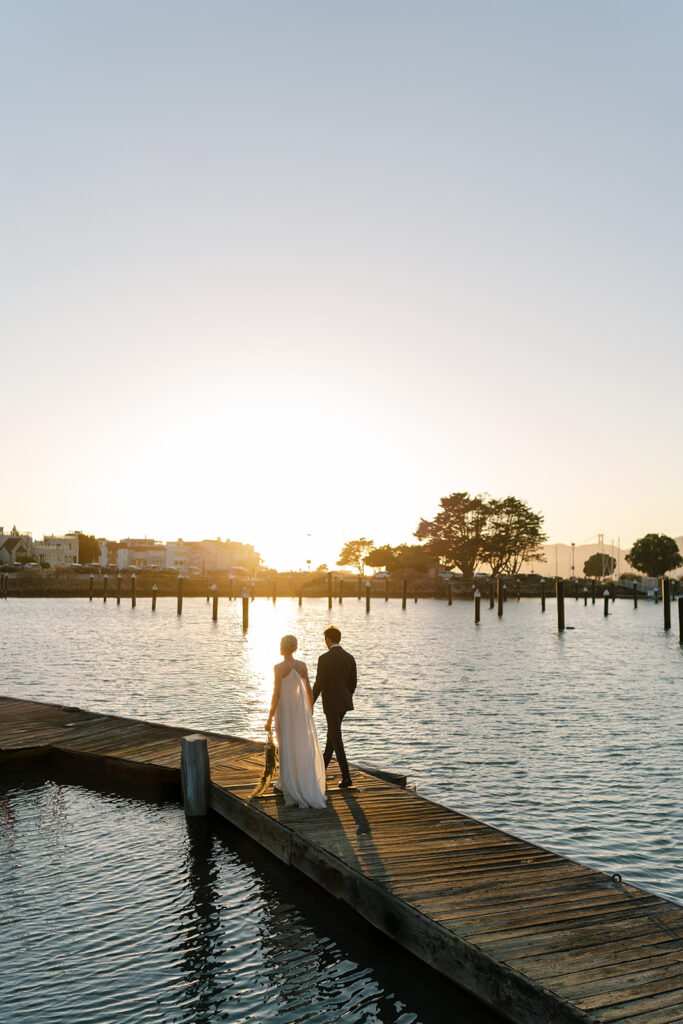 Bride and groom walking on a dock in the bay as the sunsets over them