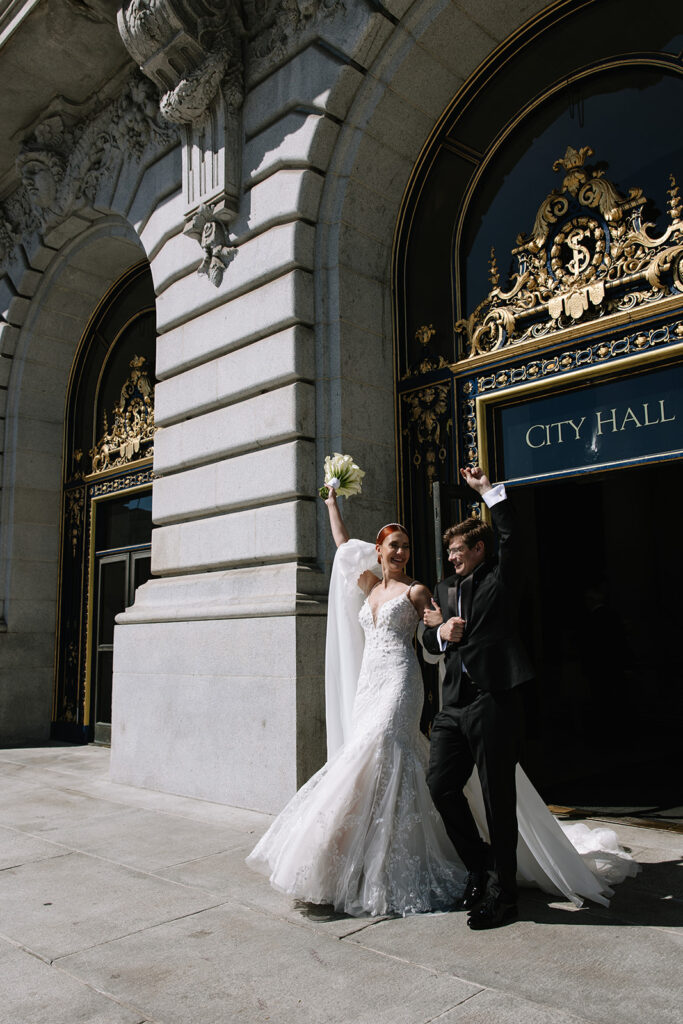 Bride and groom exiting city hall waving their hands and bouquet in the hair