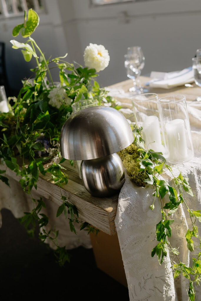 sweetheart table with draped linens, green cascading florals, candles, and a silver lamp in front of open windows