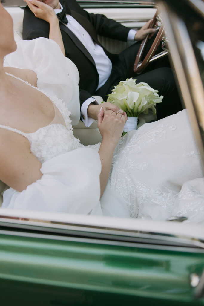 Groom and bride sitting in the car holding hands while she touches his face