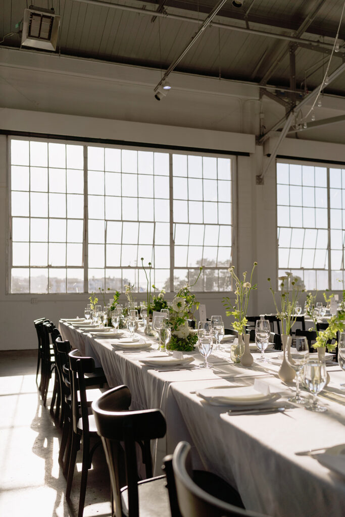 large warehouse indoor wedding reception with green florals lining the tables