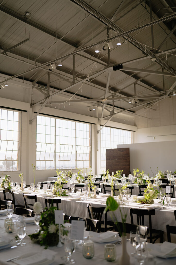 large warehouse indoor wedding reception with green florals lining the tables