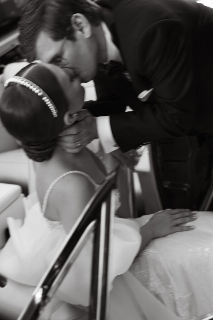 Film photo of bride sitting in driver seat with door open as groom pulls her in for a kiss