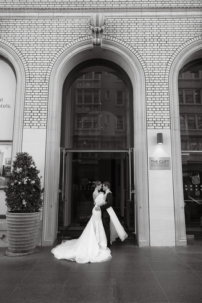 Bride and groom nose to nose in front of their hotel, the cliff.