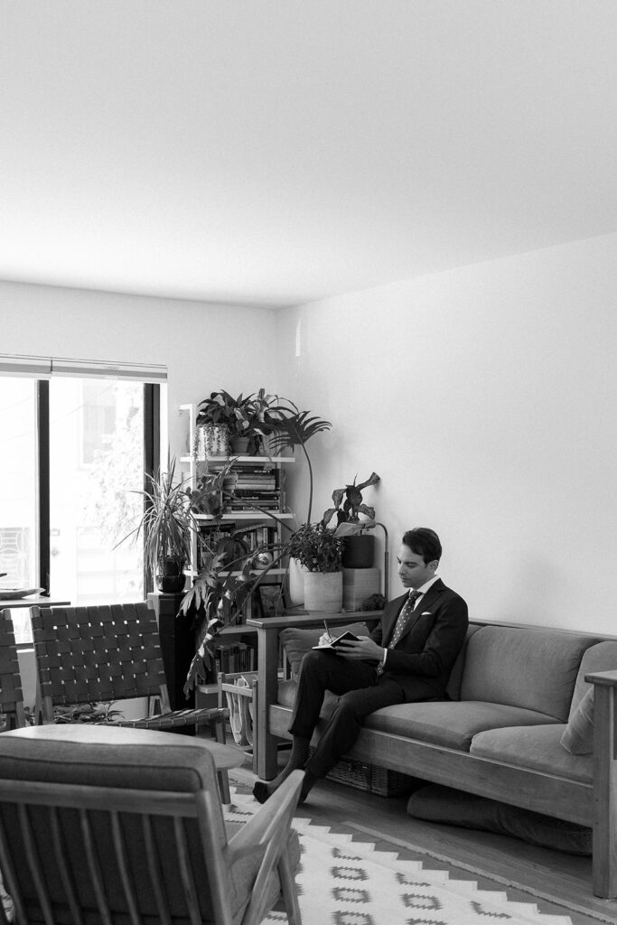Groom sitting on couch writing in a journal.