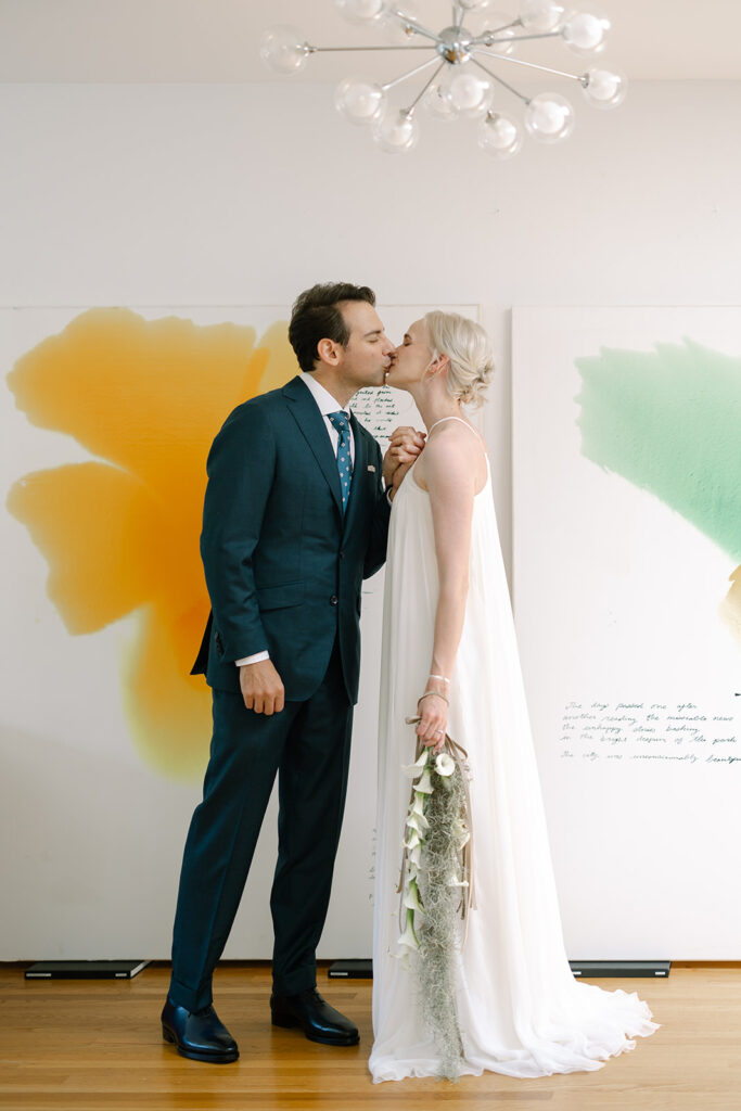 bride and groom kissing in front of two art prints sitting on the floor.