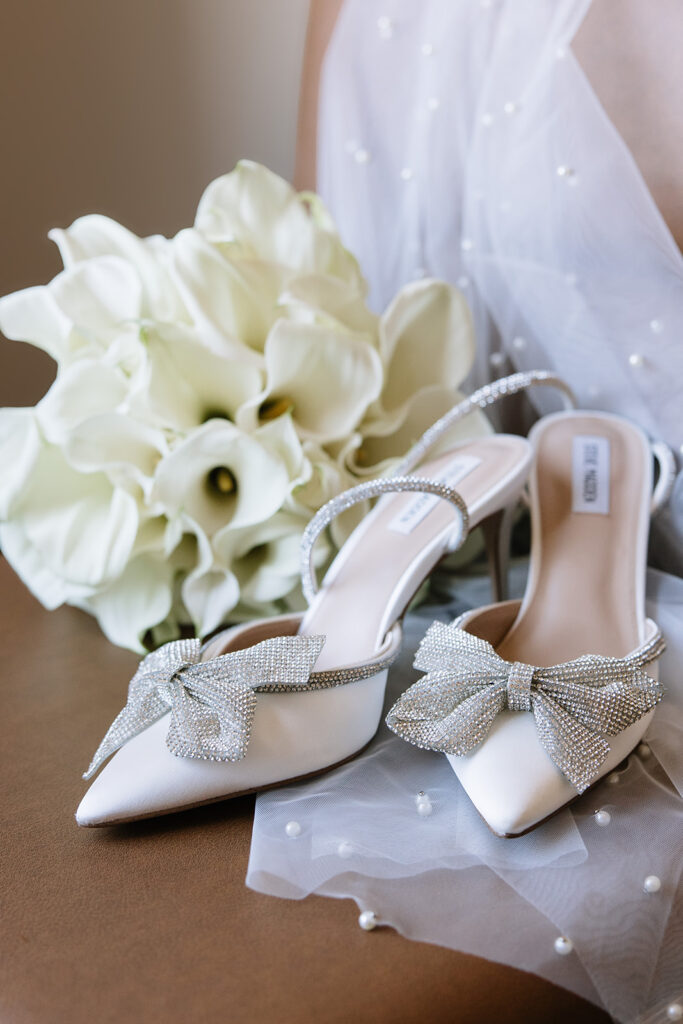Bridal details with her designer bow heels, white calla lily bouquet, and pearl veil.