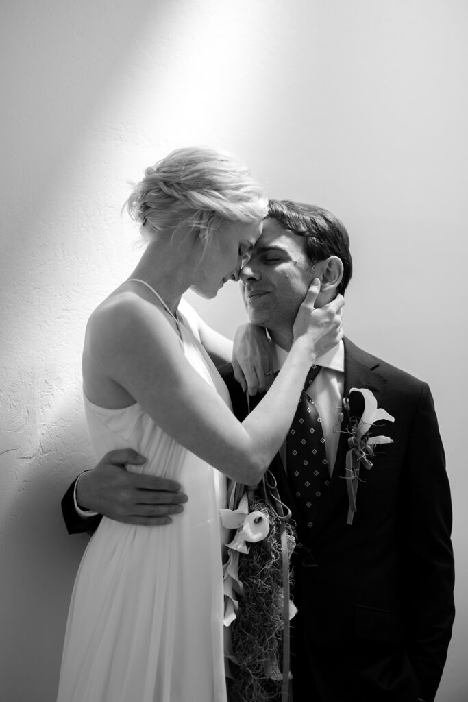 Bride and groom embracing while touching foreheads and lily wedding florals