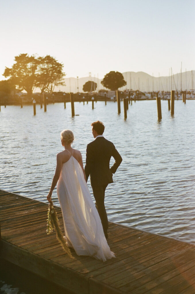 Bride and groom walking on a dock in the bay as the sunsets over them on film