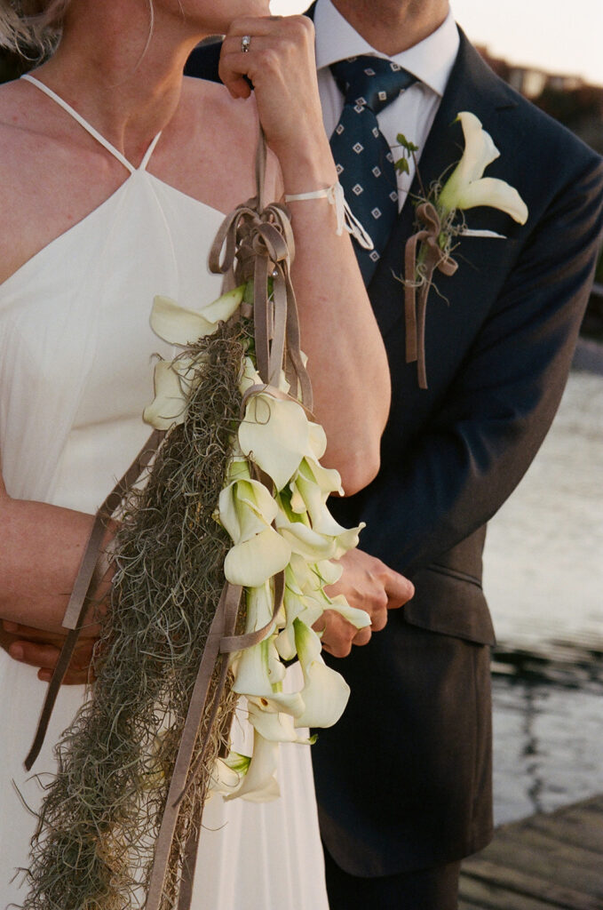 Bridal wrist bouquet with calla lilies and mossy hanging florals and a brown velvet ribbon that matches the grooms lili boutonniere