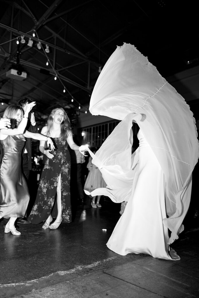 Bride fanning her long wedding gown sleeves on the dancefloor.