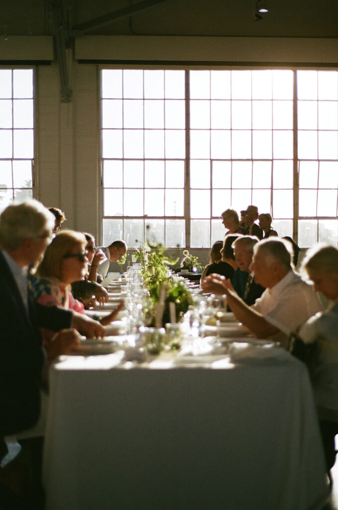 Down the line of the wedding reception table of guests chatting captured on film