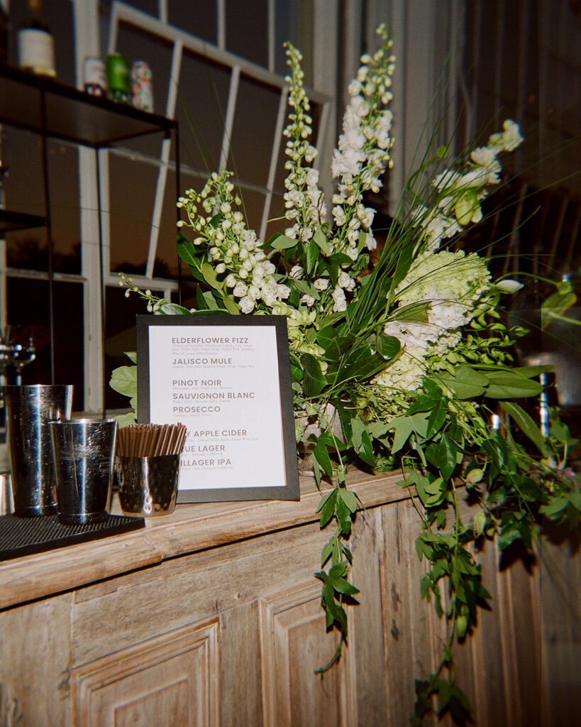Wooden bar with black and white menu and green and white floral arrangement