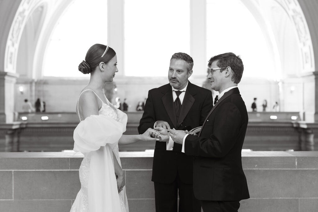Groom about to place ring on bride during wedding ceremony at SF city hall
