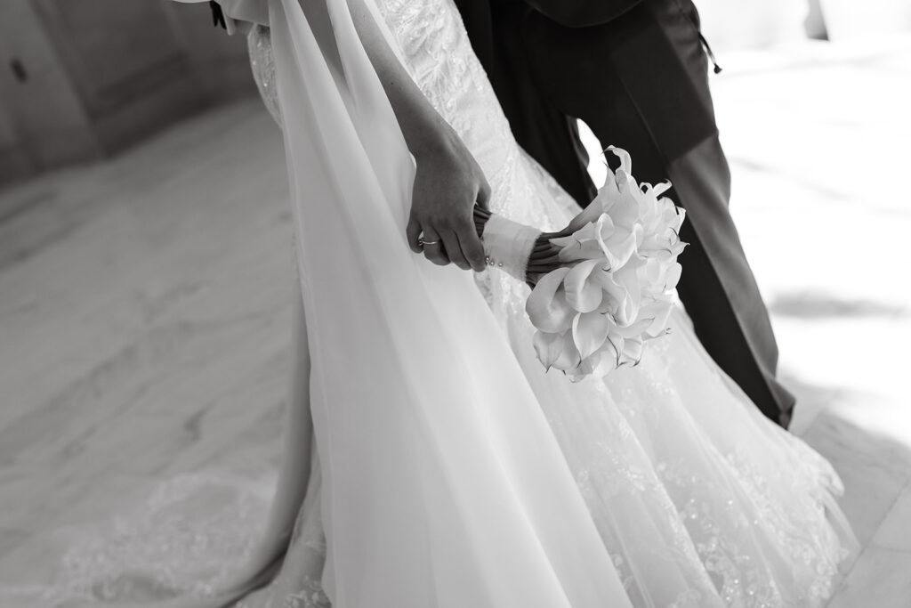 Bridal detail holding the bridal bouquet alongside her wedding gown