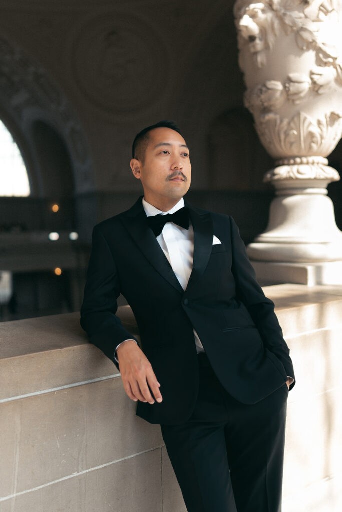 Groom leaning on wall looking off in the distance