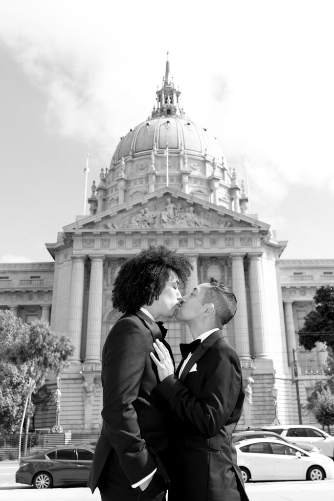Grooms kissing in front of city hall in black and white
