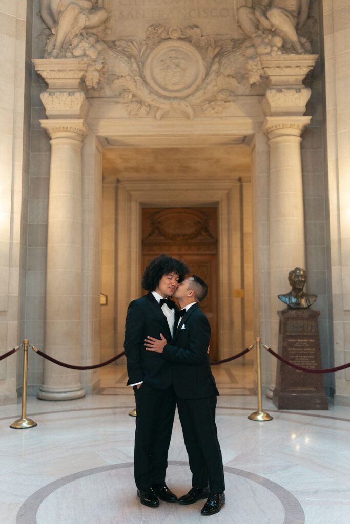 Groom kissing his husbands cheek in the rotunda of SF city hall