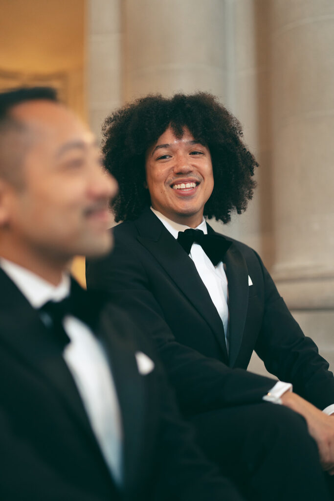 Groom in background smiling at groom in front of him out of focus