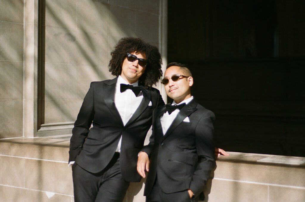 Grooms in their wedding tuxes and sunglasses as they lean on a wall in SF city hall