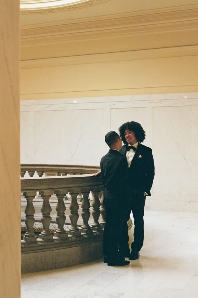 Grooms looking at each other, captured from a distance, as they lean on the balcony