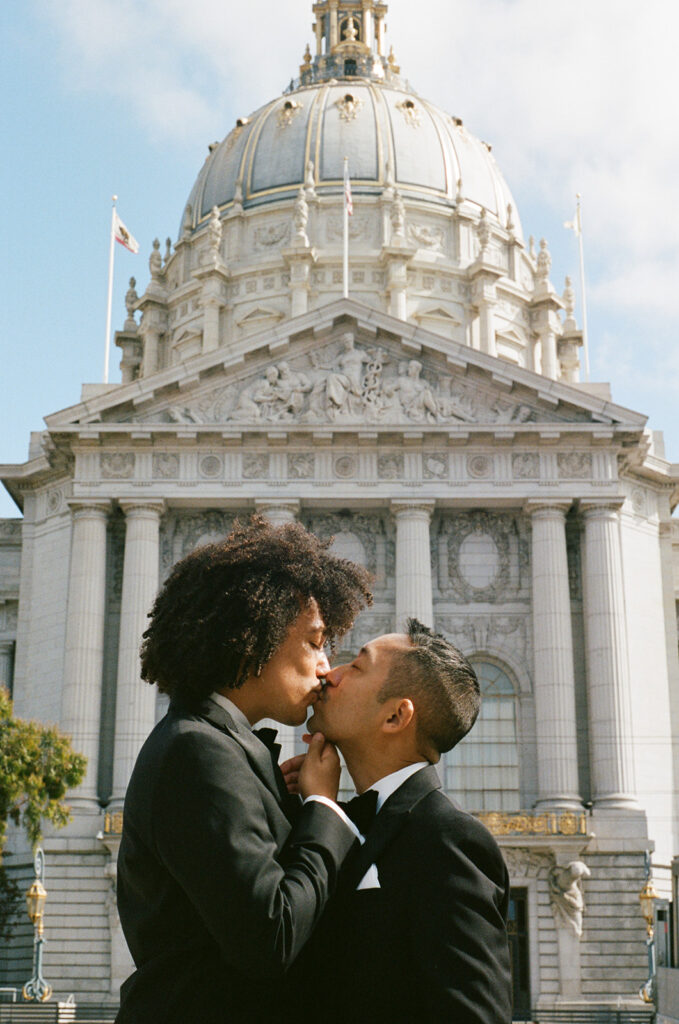 Interracial grooms kissing in front of city hall 