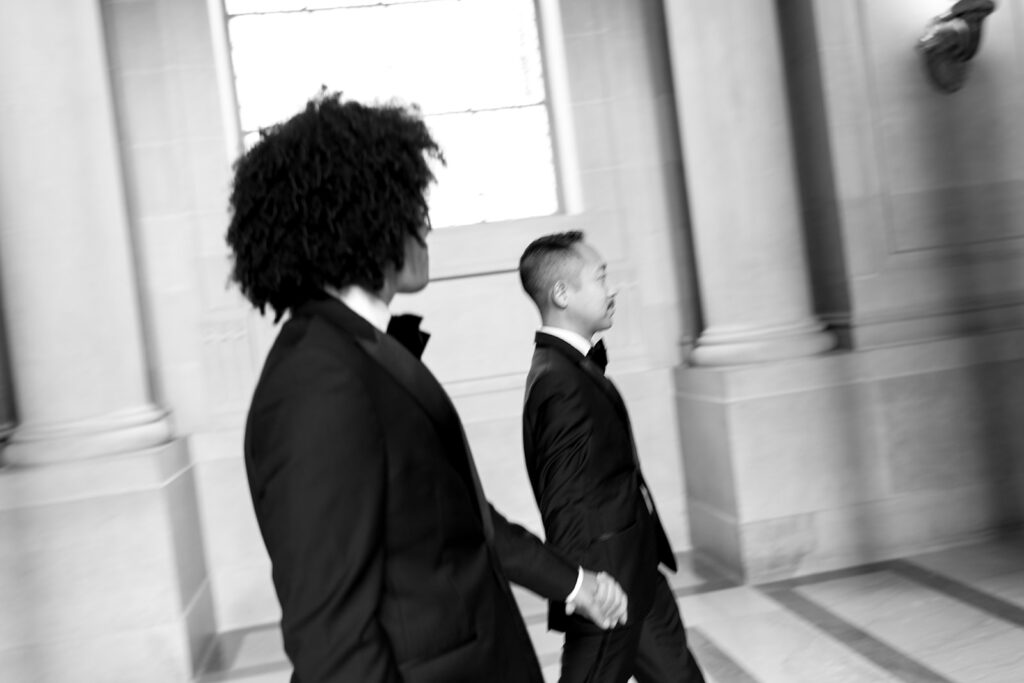 Grooms holding hands walking side by side, motion blur